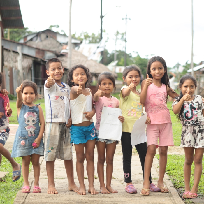 A group of smiling children giving their thumbs up stand in a line smiling outside in a Peru village.